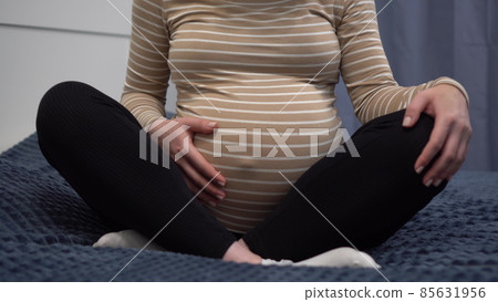 Young pregnant woman with glasses stroking her belly. The girl in the bedroom on the bed. The camera zooms in. 85631956