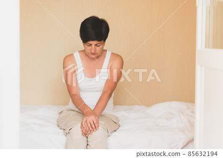 A middle-aged woman is sitting in bed, depressed. Women's health depression sleep problems sadness loneliness. 85632194