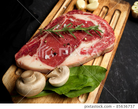 Marbled raw beef steak with seasoning on a wooden board. Marbled raw beef steak with seasoning on a wooden board. 85636737