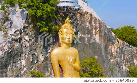Aerial view of Phra Putthachai Tham Rusi Khao Ngu, golden buddha pagoda stupa, Ratchaburi, Thailand with green mountain hills and forest trees. Thai buddhist temple architecture. Tourist attraction. Aerial view of Phra Putthachai Tham Rusi Khao Ngu, golden buddha pagoda stupa, Ratchaburi, Thailand with green mountain hills and forest trees. Thai buddhist temple architecture. Tourist attraction. 85640089