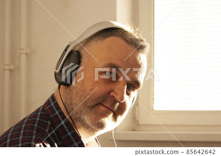 A man of European appearance in a plaid shirt in large headphones looks into the camera 85642642
