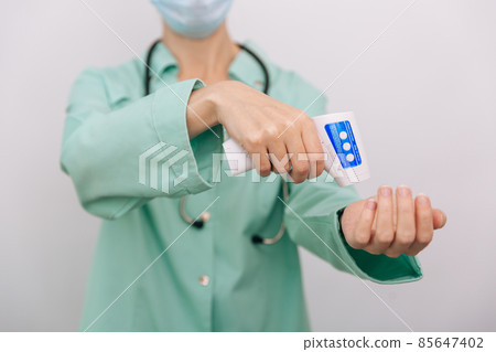 Temperature measurement gun in doctor hands. Close-up shot of doctor wearing protective surgical mask ready to use infrared isometric thermometer gun to check body temperature for virus symptoms. Temperature measurement gun in doctor hands. Close-up shot of doctor wearing protective surgical mask ready to use infrared isometric thermometer gun to check body temperature for virus symptoms. 85647402