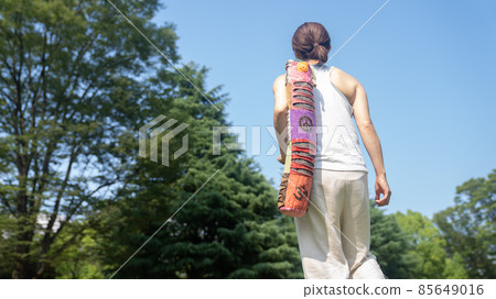 A woman heading to practice with a yoga mat A woman heading to practice with a yoga mat 85649016