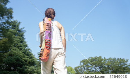 A woman heading to practice with a yoga mat 85649018