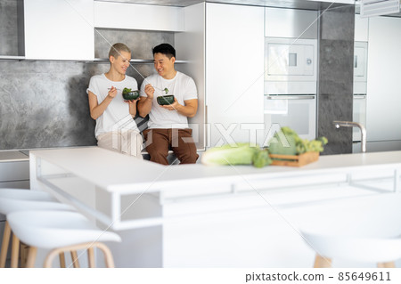 Laughing couple eating salad on kitchen at home Laughing couple eating salad on kitchen at home 85649611