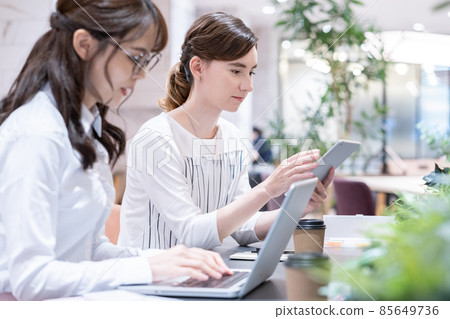 Two young women working side by side in the office 85649736