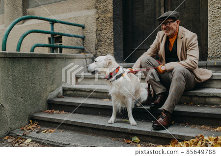 Happy senior man sitting on stairs and resting during dog walk outdoors in city. Happy senior man sitting on stairs and resting during dog walk outdoors in city. 85649788