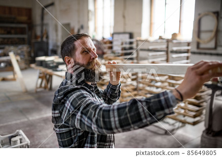 Mature male carpenter carrying wooden board indoors in carpentery workshop. Small business concept. 85649805