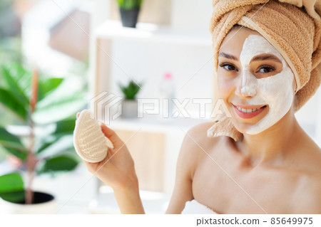 Beautiful young woman with towel wrapped around her head applying face mask at the bathroom 85649975