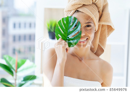 Close up of smiling woman applying coffee scrub on face 85649976