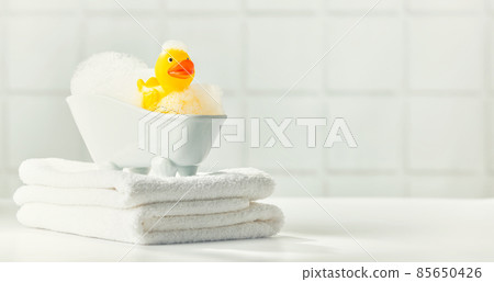 A miniature bubble bath, yellow rubber duck and white towels on bathroom countertop, children bath accessories, baby care 85650426