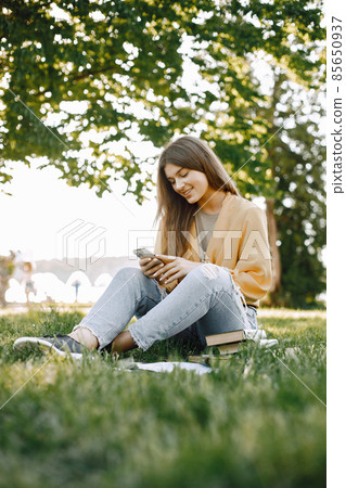 Female caucasian student sitting on a grass and using a smartphone Female caucasian student sitting on a grass and using a smartphone 85650937