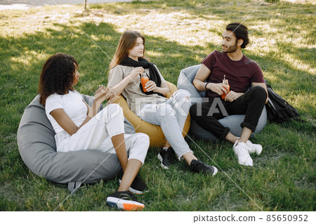 Three friends talking while sitting on the bean bag chairs in a park Three friends talking while sitting on the bean bag chairs in a park 85650952