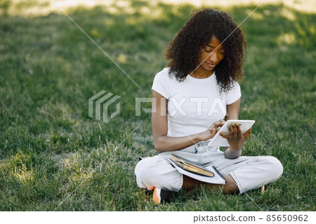 Female african student sitting on a grass and using a tablet Female african student sitting on a grass and using a tablet 85650962