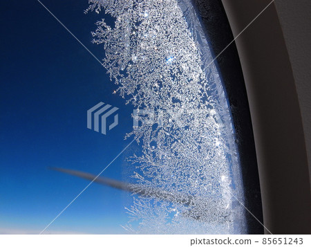 Photo 2 where the pattern of small ice crystals on the window frame of a jet plane shines in the morning sun against the background of the blue sky 85651243