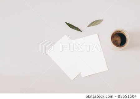 Blank greeting cards and olive tree leaves on beige background. Wedding invitations mockups scene. Cup of coffee. Breakfast concept. Flat lay, top overhead view. Working table with office equipment. 85651504