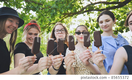 Friends hold chocolate ice cream on a stick in a row. 85655372