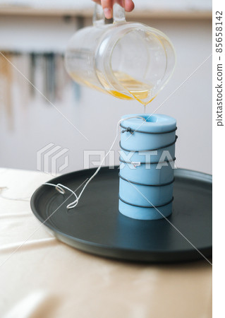 Vertical cropped shot of unrecognizable female artisan pouring yellow liquid wax from glass bowl into silicon mold. 85658142