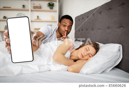 Black guy using smartphone while his girlfriend sleeping, mockup Black guy using smartphone while his girlfriend sleeping, mockup 85660626