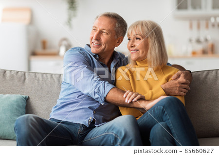 Happy Mature Spouses Hugging Looking Aside Sitting On Couch Indoor Happy Mature Spouses Hugging Looking Aside Sitting On Couch Indoor 85660627