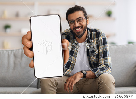 Cheerful Indian Guy Showing Smartphone With Big Blank White Screen At Camera Cheerful Indian Guy Showing Smartphone With Big Blank White Screen At Camera 85660877