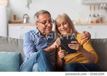 Mature Husband And Wife Using Tablet Embracing Sitting At Home 85661094