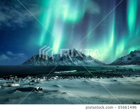 Aurora borealis, Northern lights over snow mountain range on coastline at Skagsanden beach, Lofoten islands 85661496