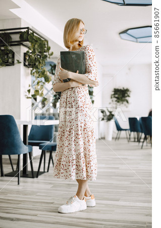 Young blonde woman standing in a cafe and holding some documents 85661907