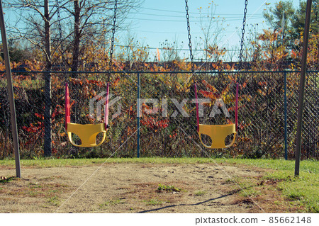 Bright yellow and red chain swings on kids playground. Autumn leaves. Covid restrictions Bright yellow and red chain swings on kids playground. Autumn leaves. Covid restrictions 85662148