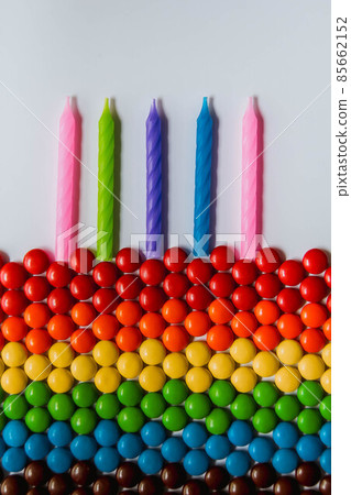Rainbow of multicolored sweet candy dragees in shape of cake with candles on white background. Creative composition of round candy dragees in Rainbow colors. Concept birthday. Top view. Flat lay 85662152