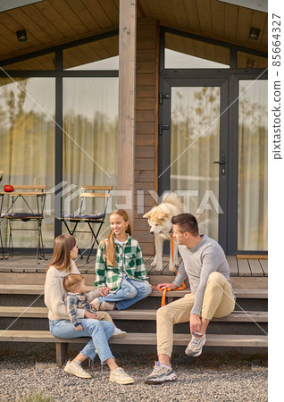 Parents looking at their daughter communicating on steps of house 85664327