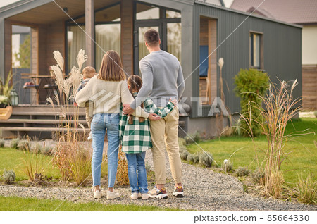 Back view of family hugging and admiring their home 85664330