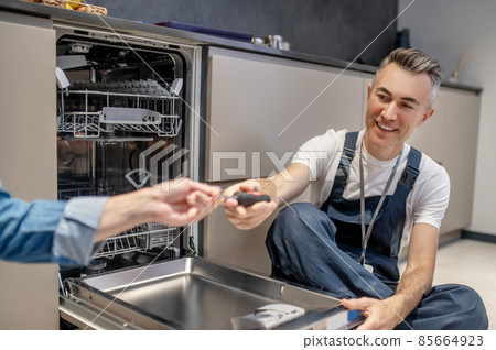 Hand holding out tool to plumber sitting on floor 85664923