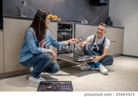 Woman holding out tool to plumbing near dishwasher 85664924