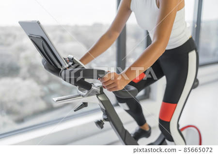 Exercise at home on spin bicycle fitness workout with screen. Woman training on stationary bike watching online video class for exercising cardio 85665072