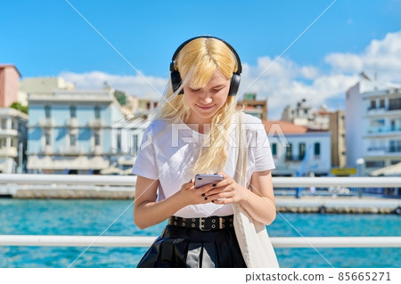 Teenage female in headphones with smartphone on the embankment Teenage female in headphones with smartphone on the embankment 85665271