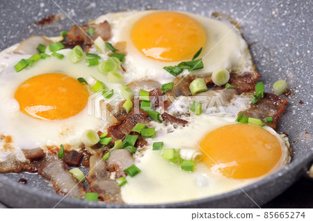 fried eggs with bacon and green onions in a frying pan 85665274
