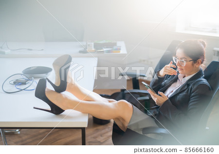 Business woman put feet on work desk and uses mobile phone in office Business woman put feet on work desk and uses mobile phone in office 85666160