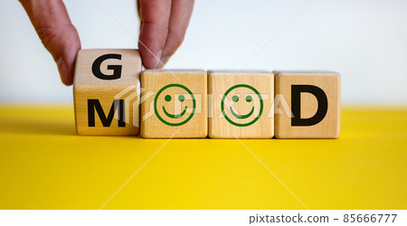 Good mood symbol. Male hand flips a wooden cube and changes the word 'good' to 'mood'. Positive smiles. Beautiful yellow table, white background, copy space. Business and good mood concept. 85666777