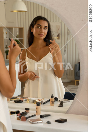 brunette woman with long straight dark hair and clean skin doing make up routine brunette woman with long straight dark hair and clean skin doing make up routine 85666860
