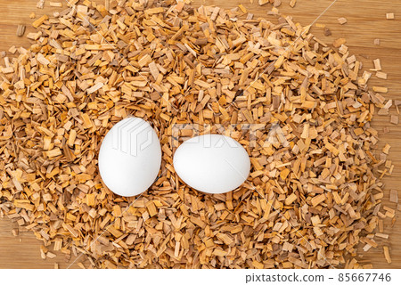 Top view of two white chicken eggs in sawdust on a wooden table. Top view of two white chicken eggs in sawdust on a wooden table. 85667746