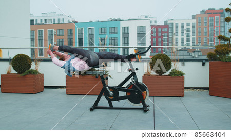 Caucasian woman coach making stretching aerobic training exercises on stationary bike outdoors Caucasian woman coach making stretching aerobic training exercises on stationary bike outdoors 85668404
