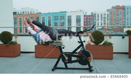 Athletic woman makes twine training routine on spinning stationary bike on house roof, weight loss Athletic woman makes twine training routine on spinning stationary bike on house roof, weight loss 85668405