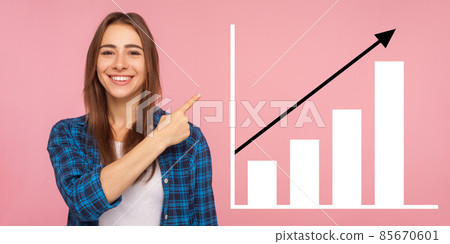 Portrait of happy joyful young woman standing, pointing aside and showing business growth graph. indoor studio shot isolated on pink background Portrait of happy joyful young woman standing, pointing aside and showing business growth graph. indoor studio shot isolated on pink background 85670601