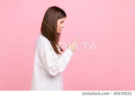 Side view portrait of strict female with raised finger, showing warning gesture, scolding somebody, wearing white casual style sweater. Indoor studio shot isolated on pink background. Side view portrait of strict female with raised finger, showing warning gesture, scolding somebody, wearing white casual style sweater. Indoor studio shot isolated on pink background. 85670832