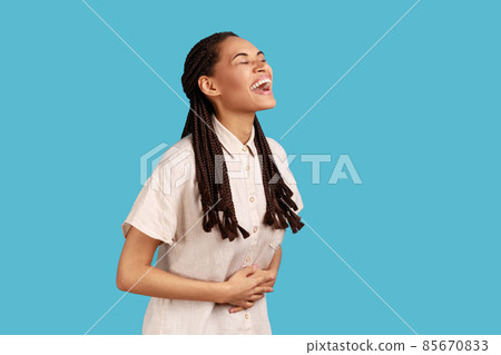 Portrait of happy beautiful woman with black dreadlocks laughing out loud, hearing funny joke, expressing positive, wearing white shirt. Indoor studio shot isolated on blue background. Portrait of happy beautiful woman with black dreadlocks laughing out loud, hearing funny joke, expressing positive, wearing white shirt. Indoor studio shot isolated on blue background. 85670833