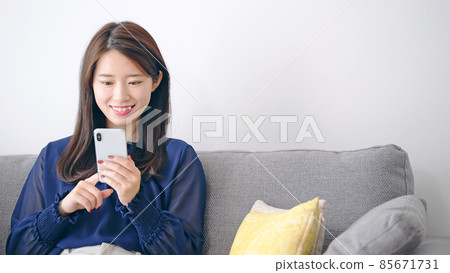 A woman relaxing in the room and looking at her smartphone A woman relaxing in the room and looking at her smartphone 85671731