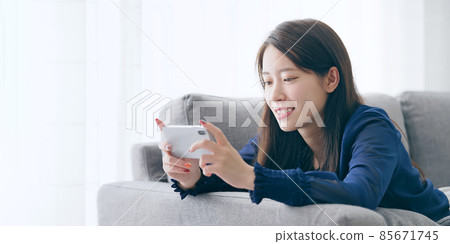 一個女人躺在沙發上,看著她的智能手機 一個女人躺在沙發上,看著她的智能手機 85671745