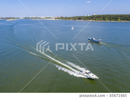 The boat rushes towards the ship on a wide river near the forest on a sunny summer day 85671985