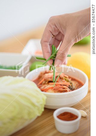 The chef is decorating kimchi with fresh vegetables. 85674477